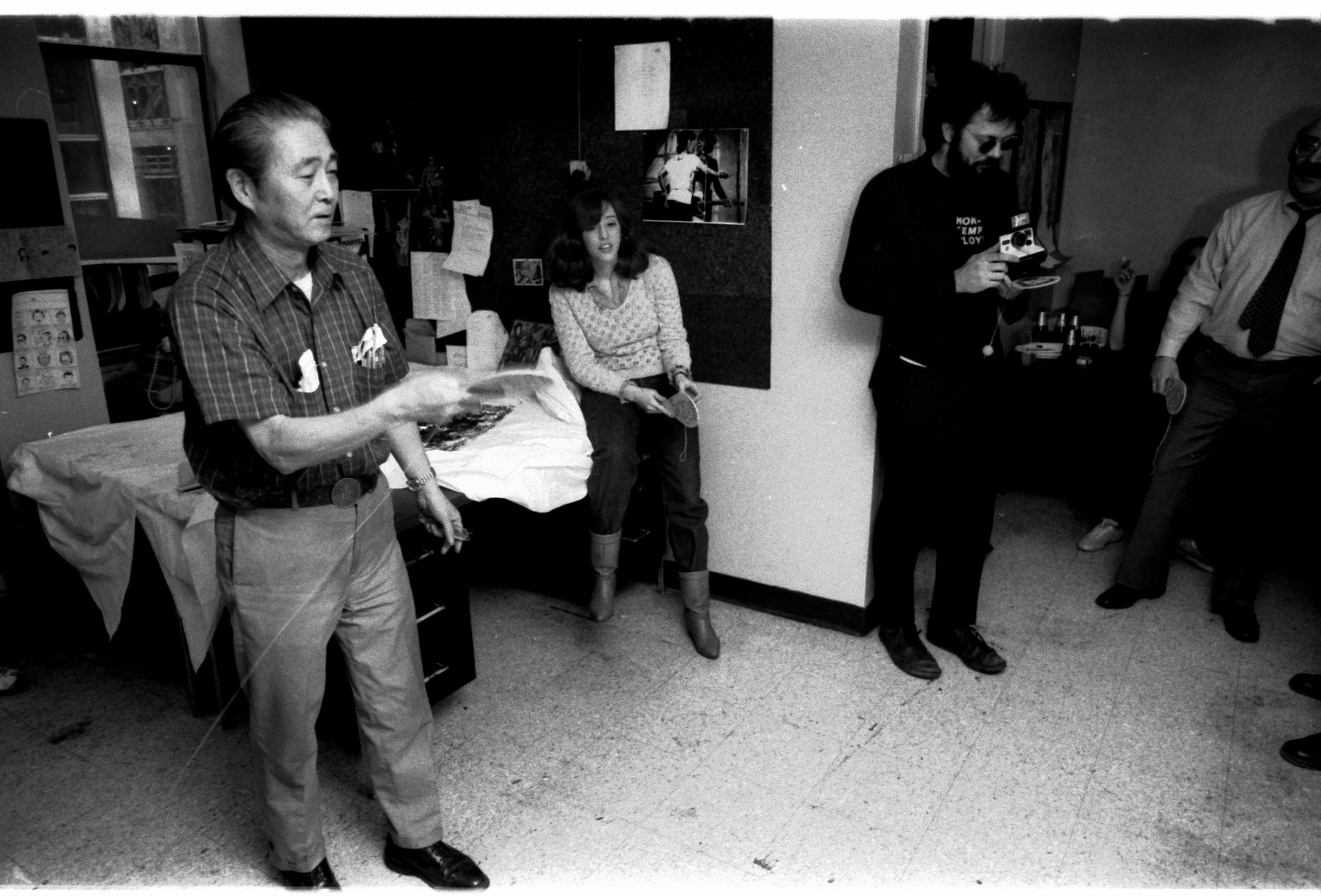Morrie Kuramoto displaying the cool, calm collection that made him famous in the Marvel Bullpen. Rick Parker-- the Man in Black-- is holding a Polaroid instant print camera, but is not using it as those shots are expensive.