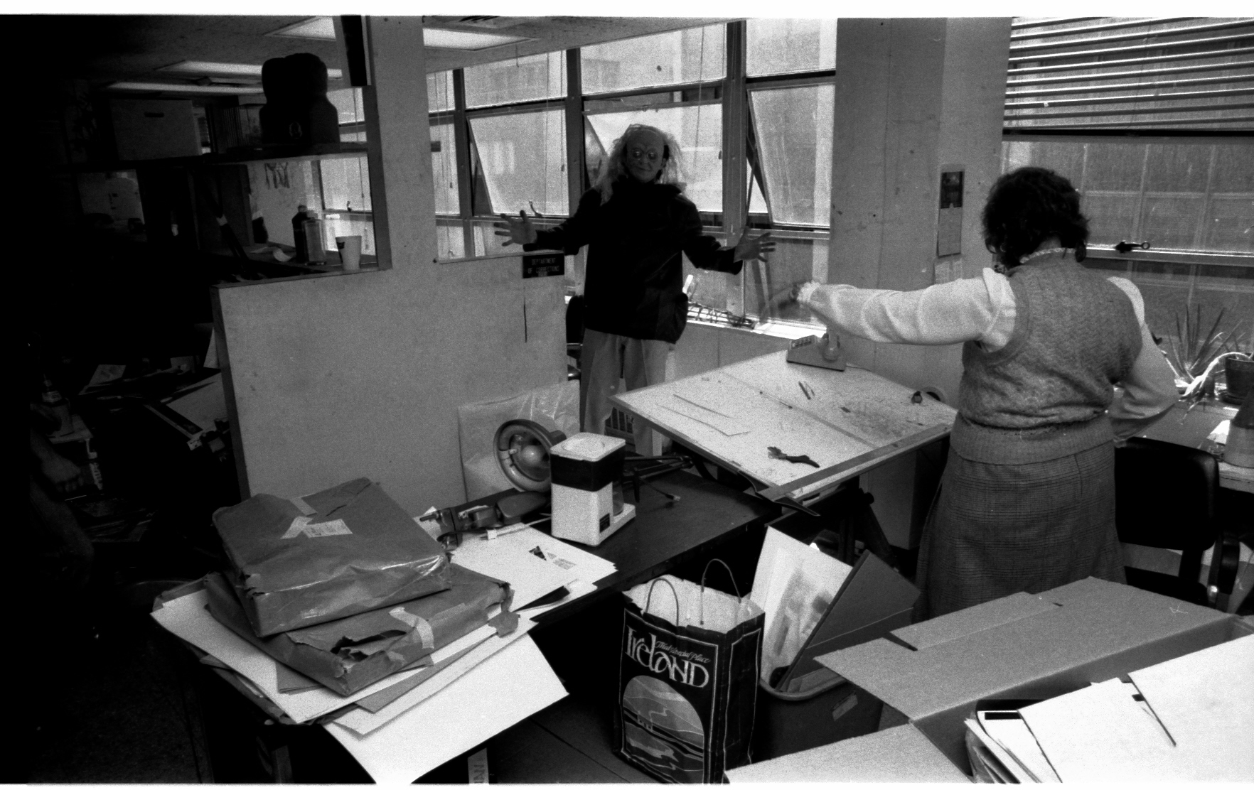 The window wall of the Bullpen. We were clearly moving that day! Davida Lichter-Dale sports a horror mask-- no doubt taken from Rick Parker's desk which she is standing next to. Nora Maclin conducts.