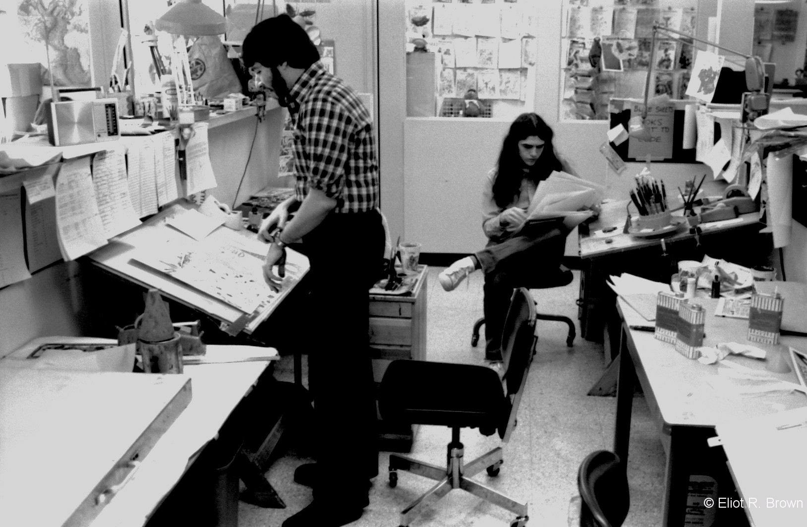 The Marvel Bullpen, located at 575 Madison Avenue, between 56 & 57 Streets on the 6th Floor. Joe Albelo standing and Mike Higgins contemplating a sheaf of art boards. C. 1979