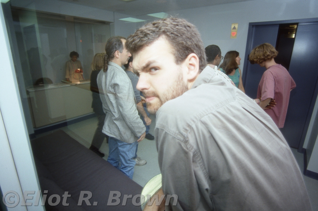 Seen through an architecturally necessary wall of security glass is the suspicious side of Rob Tokar! Noteworthy is another wall of security glass is Receptionist Supreme Erica Mitchell caught in a pensive pose and to the image right with his trademark sprayof blonde hair, Assistant Editor Kevin Somers.